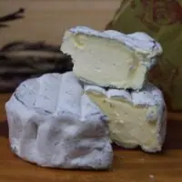 Cunha farta do Queijo Lua Cheia cremoso exibindo sua fina camada de carvão vegetal sob a casca branca.