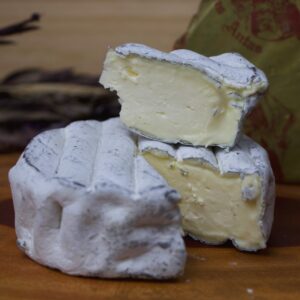 Cunha farta do Queijo Lua Cheia cremoso exibindo sua fina camada de carvão vegetal sob a casca branca.