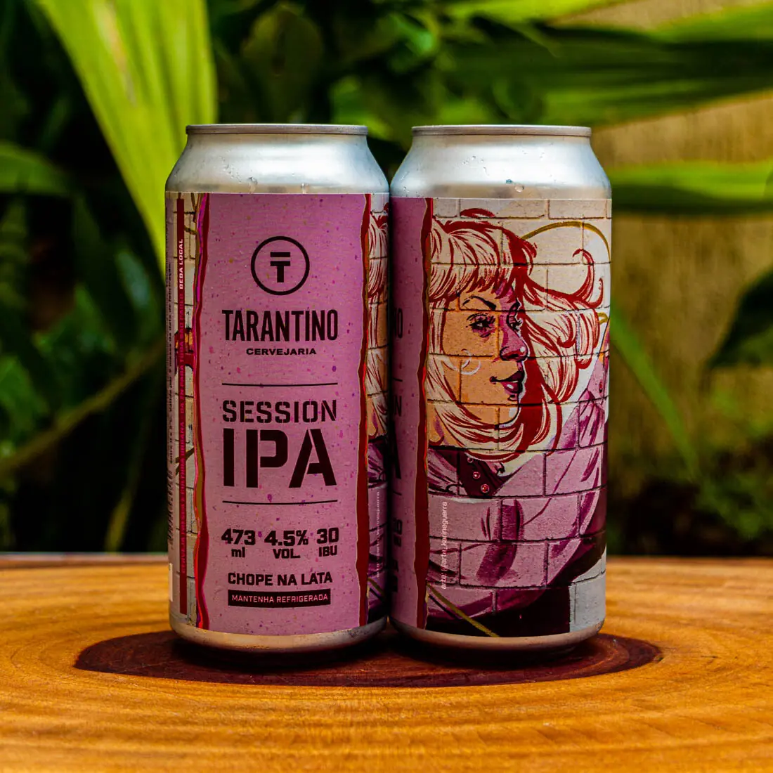 Duas latas da Cerveja Session IPA da Cervejaria Tarantino, com seu rótulo artístico e urbano em destaque sobre uma base de madeira.