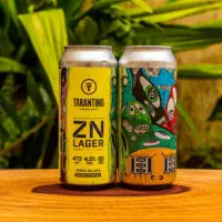Duas latas da cerveja artesanal ZN Lager da Cervejaria Tarantino, com rótulo amarelo vibrante e arte urbana colorida na lateral.