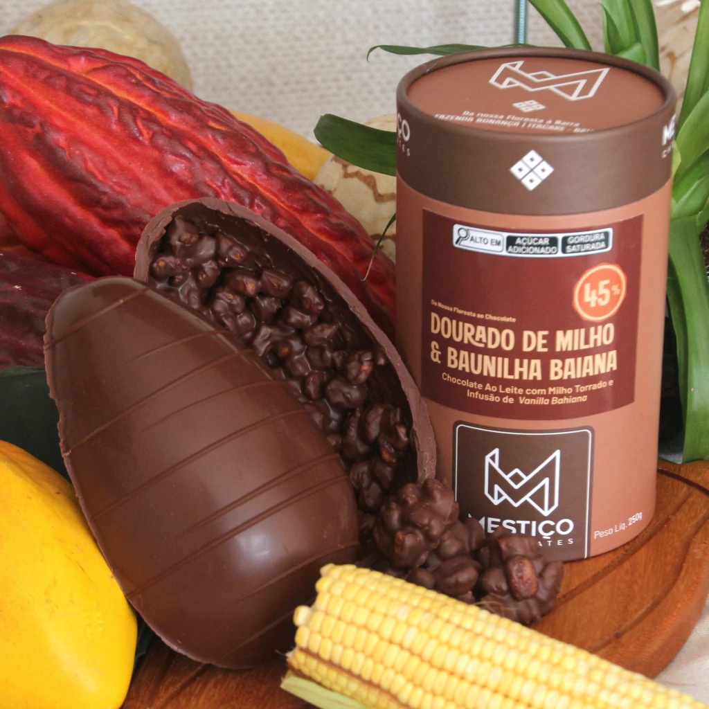 Ovo de Páscoa Mestiço 45% aberto mostrando recheio de milho torrado e baunilha baiana com espiga de milho ao lado.