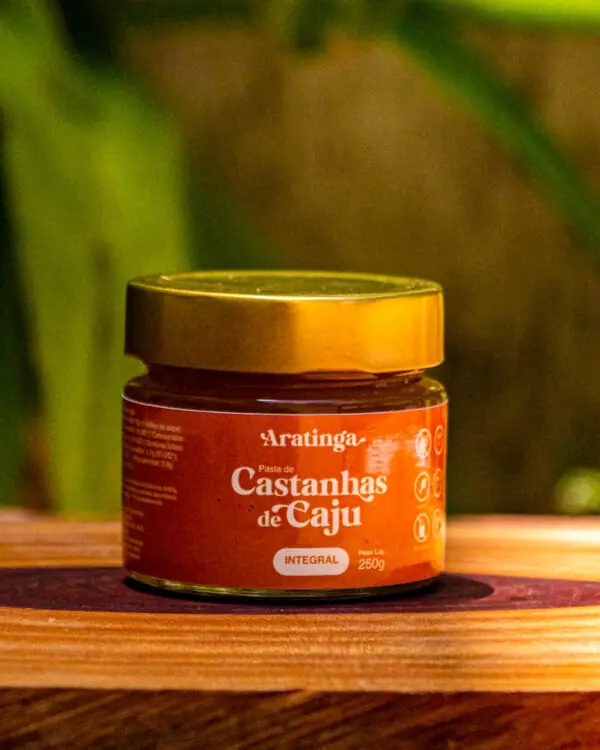 Pote de vidro da Pasta de Castanhas de Caju Integral Aratinga de 250g sobre uma base rústica de madeira.