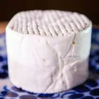 Queijo Frescal artesanal Fazenda Atalaia redondo de massa branca com textura marcada sobre prato decorado azul.