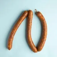 Linguiça Merguez bovina picante da FA Defumados sobre tábua de madeira rústica.