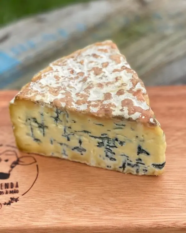 Fatias e cunha do cremoso Queijo Mofo Azul Duzu da BelaFazenda descansando sobre rústica tábua para cortes em sítio.