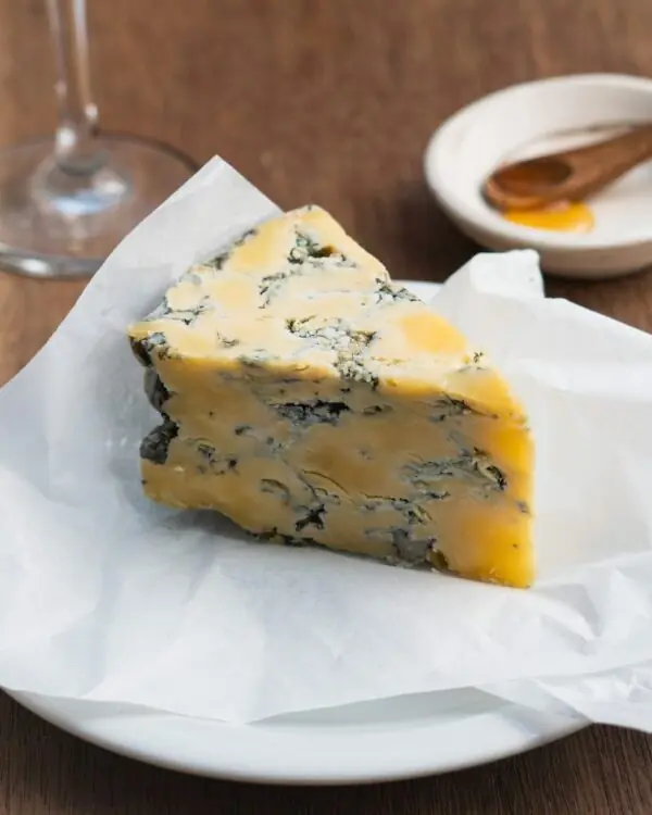 Deslumbrante e sedutora fatia de curado e úmido Queijo Azul Britânia da BelaFazenda descansando à frente a pires de degustação de Mel.