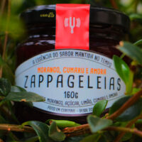 Pote de Geleia Zappa entre folhagens verdes com ingredientes naturais visíveis no rótulo Pote de Geleia Zappa entre folhagens verdes com ingredientes naturais visíveis no rótulo