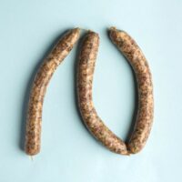 Linguiça do Sertão artesanal com pimenta biquinho da FA Defumados sobre tábua rústica.