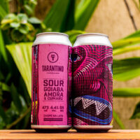 cerveja-sour-goiaba-amora-e-cumaru-cervejaria-tarantino-473ml-1 Duas latas da Cerveja Sour Goiaba, Amora e Cumaru da Tarantino, com o rótulo rosa e a arte psicodélica em destaque sobre uma base de madeira.
