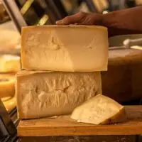 Peças de Queijo Tulha Fazenda Atalaia abertas em uma tábua, destacando a textura granular e a cor amarelo-alaranjada característica da maturação prolongada.