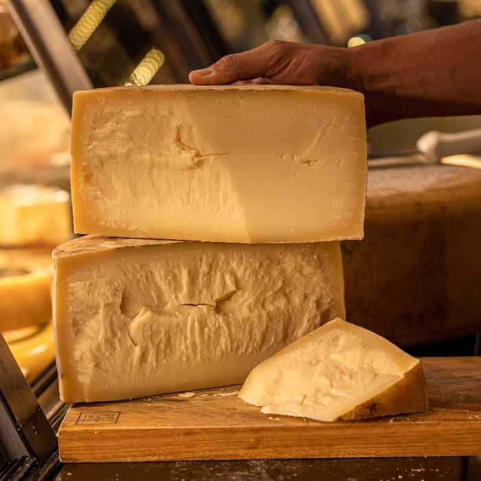 Peças de Queijo Tulha Fazenda Atalaia abertas em uma tábua, destacando a textura granular e a cor amarelo-alaranjada característica da maturação prolongada.