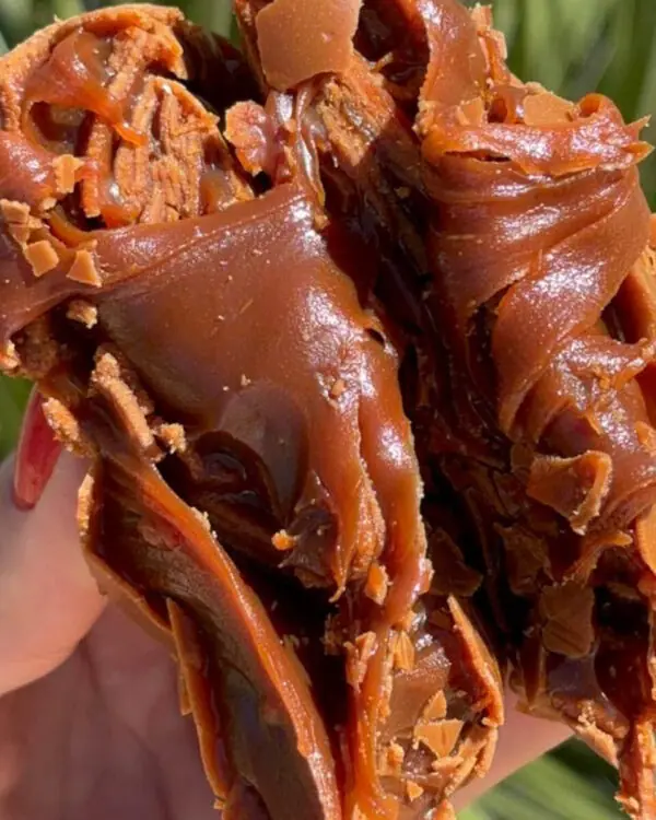 Textura cremosa e bem elástica da bala de doce de leite puxa-puxa partida ao meio, revelando interior brilhante.