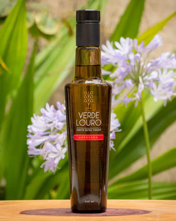 Azeite Extra Virgem Arbosana Verde Louro de 250ml, faixa vermelha da safra atualizada sobre placa de madeira e folhas verdes