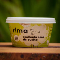Coalhada Seca de Ovelha Rima 200g sobre tábua rústica de madeira em cenário natural.