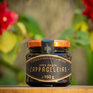 Geleia de Alho Negro Zappa Geleias pote de vidro 160g rótulo preto e dourado com tampa laranja sobre tábua de madeira