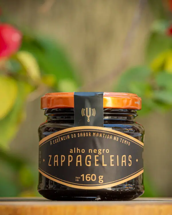 Geleia de Alho Negro Zappa Geleias pote de vidro 160g rótulo preto e dourado com tampa laranja sobre tábua de madeira