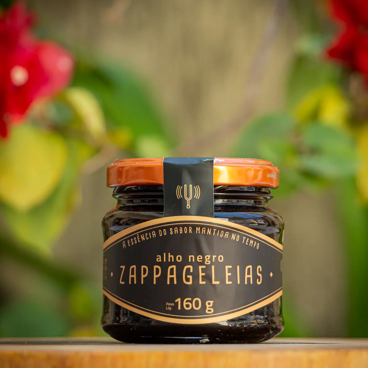 Geleia de Alho Negro Zappa Geleias pote de vidro 160g rótulo preto e dourado com tampa laranja sobre tábua de madeira