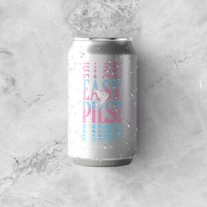 Lata de 350ml da cerveja Easy Pils! da Cervejaria Trilha, coberta de gotas de água e deitada sobre uma superfície de mármore e gelo.