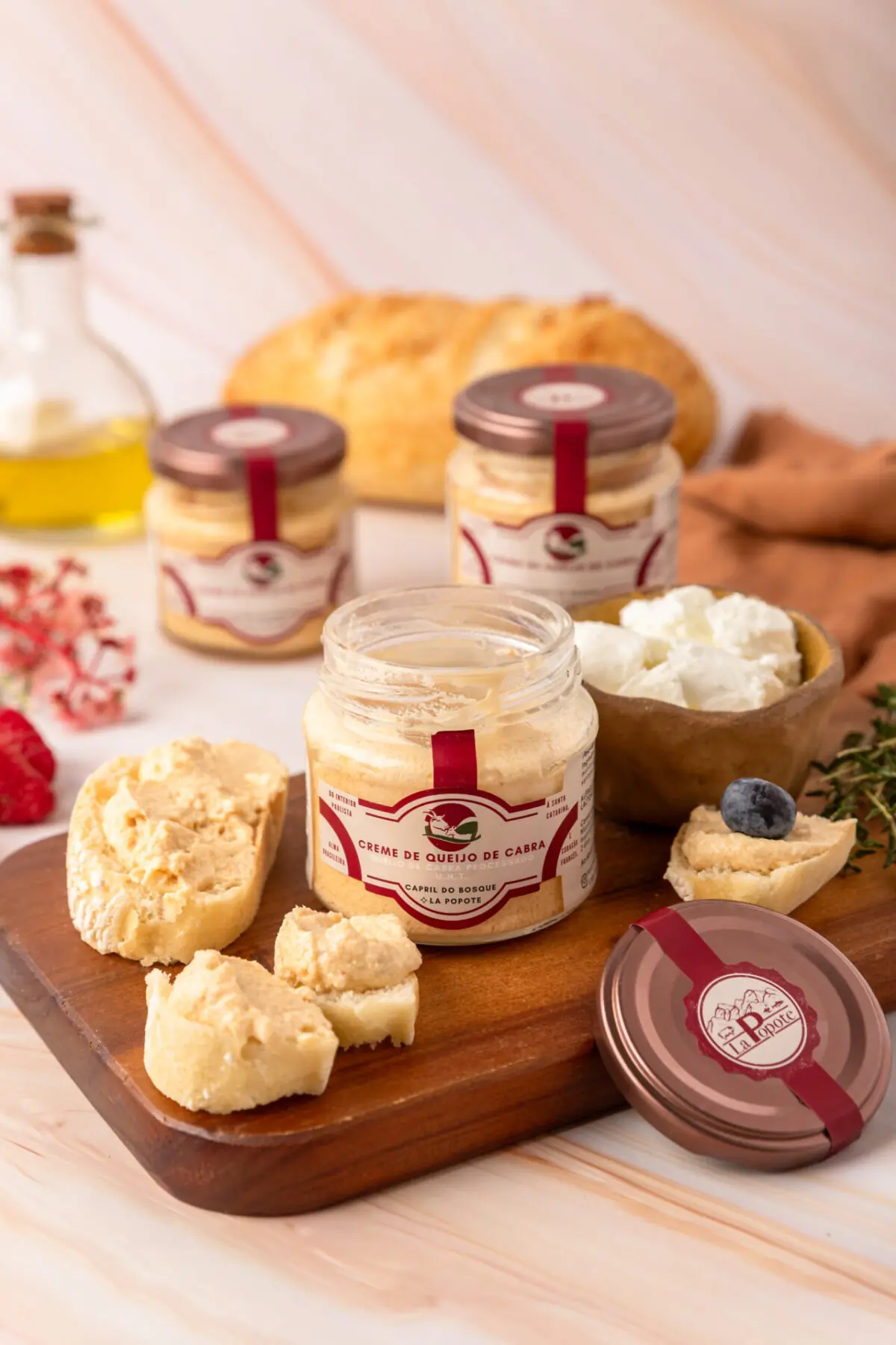 Creme de Queijo de Cabra La Popote em pote de vidro aberto, servido com espátula sobre tábua com pães artesanais e tomilhoCreme de Queijo de Cabra La Popote em pote de vidro aberto, servido com espátula sobre tábua com pães artesanais e tomilho