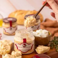Creme de Queijo de Cabra La Popote sendo servido com espátula de madeira sobre tábua de queijos artesanais com pão e tomilho fresco