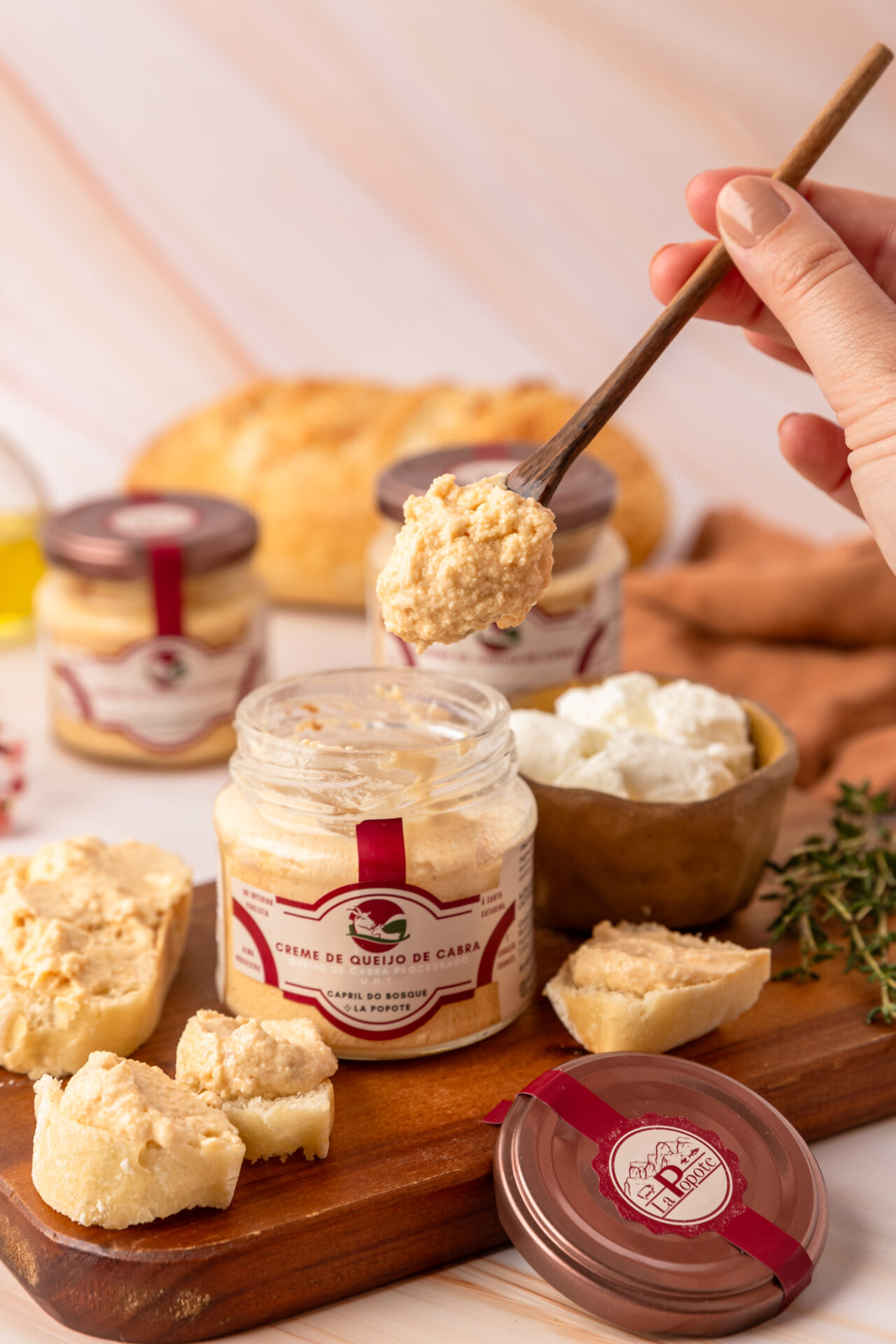 Creme de Queijo de Cabra La Popote sendo servido com espátula de madeira sobre tábua de queijos artesanais com pão e tomilho fresco