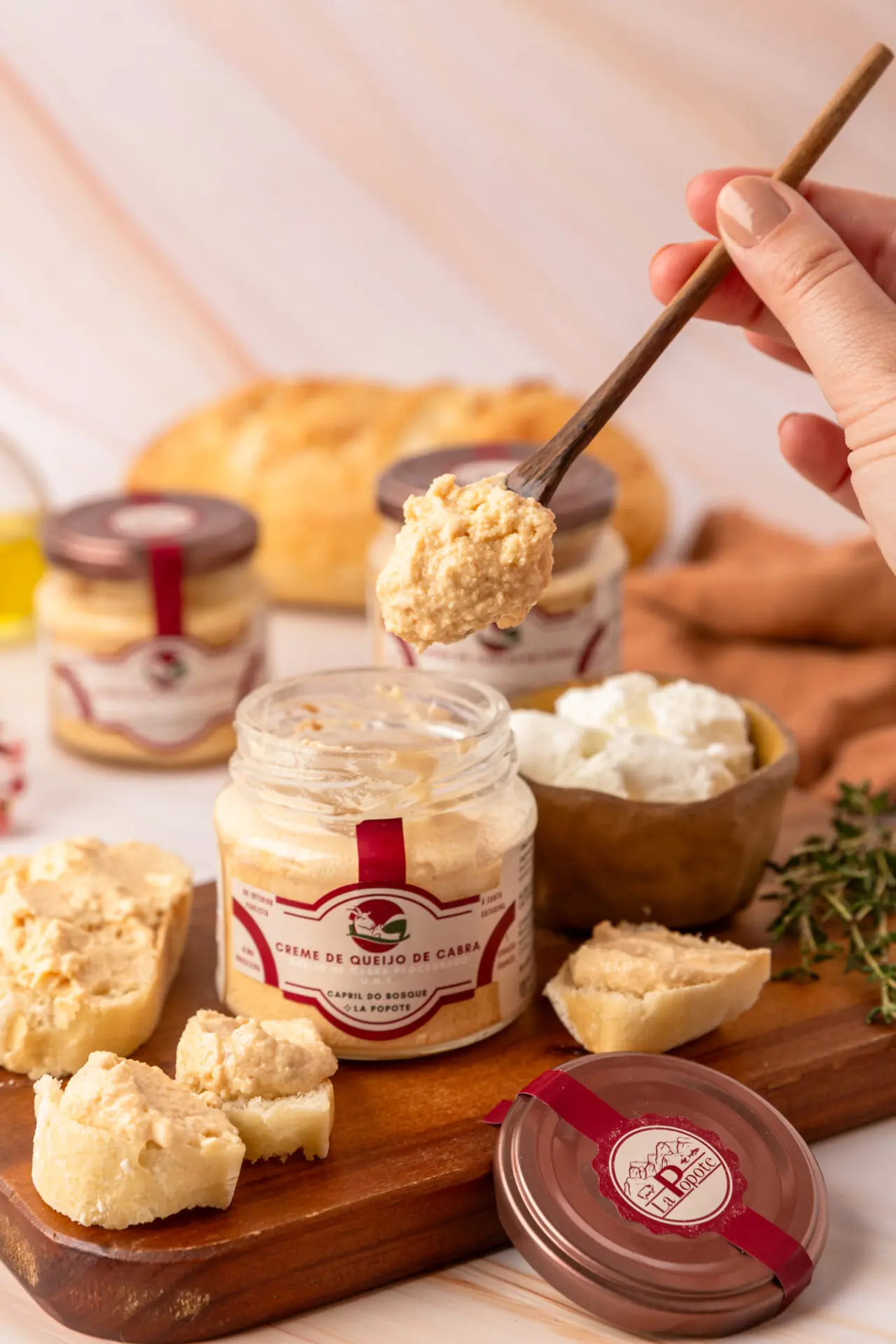 Creme de Queijo de Cabra La Popote sendo servido com espátula de madeira sobre tábua de queijos artesanais com pão e tomilho fresco