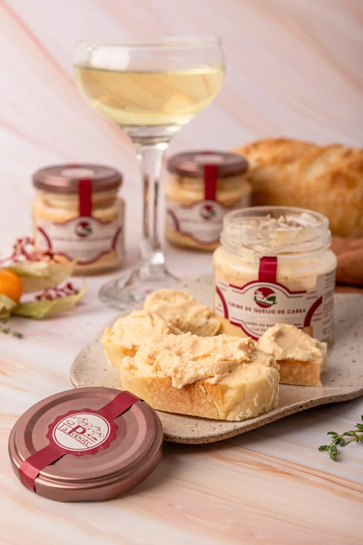 Pote de vidro do Creme de Queijo de Cabra La Popote aberto em cima de tábua rústica com pão artesanal e ervas frescas