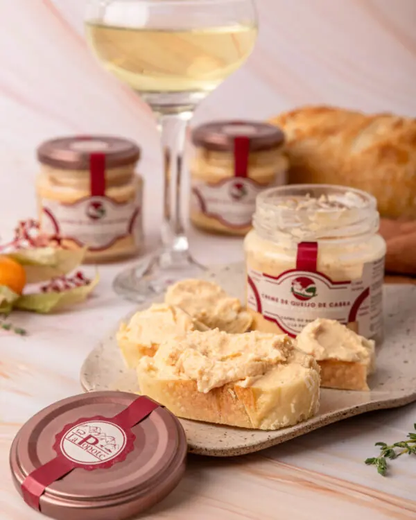 Pote de vidro do Creme de Queijo de Cabra La Popote aberto em cima de tábua rústica com pão artesanal e ervas frescas