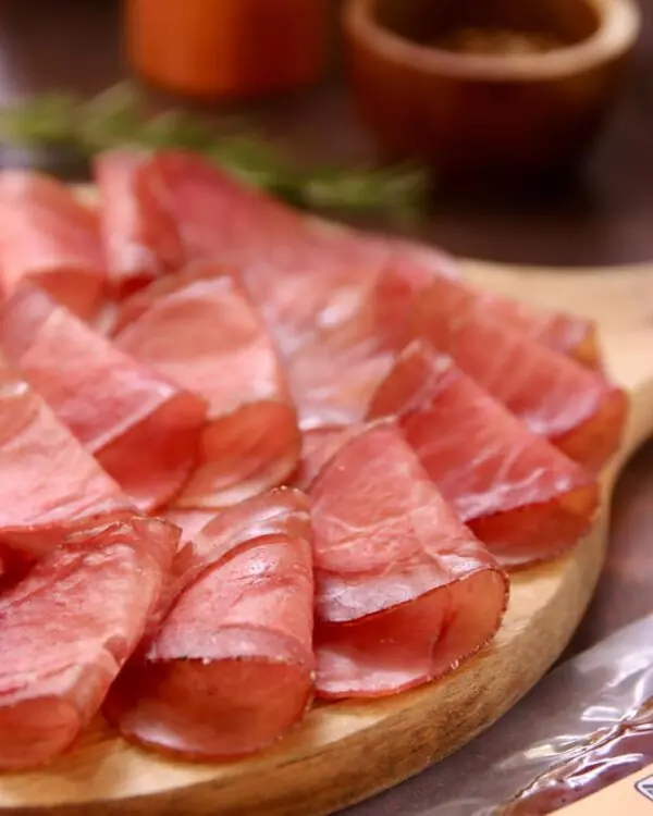 Detalhe da textura macia das fatias de lombo suíno curado (lonza) De Paula, destacando o corte uniforme. Detalhe da textura macia das fatias de lombo suíno curado (lonza) De Paula, destacando o corte uniforme.