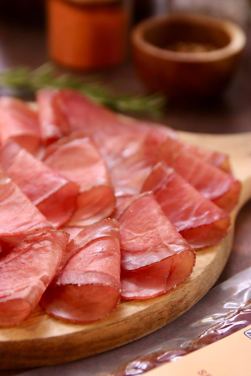 Detalhe da textura macia das fatias de lombo suíno curado (lonza) De Paula, destacando o corte uniforme.