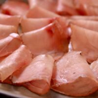 Close-up de fatias finas e rosadas de lonza artesanal dispostas em uma tábua de madeira gourmet com alecrim.