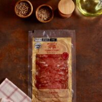Embalagem de Lonza Maturada De Paula Charcuterie 80g fatiada em cenário gastronômico rústico com azeite.
