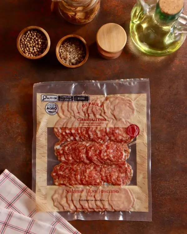 Embalagem de Salame Toscano De Paula Charcuterie 100g fatiado em cenário rústico com pimentas e temperos. Embalagem de Salame Toscano De Paula Charcuterie 100g fatiado em cenário rústico com pimentas e temperos.