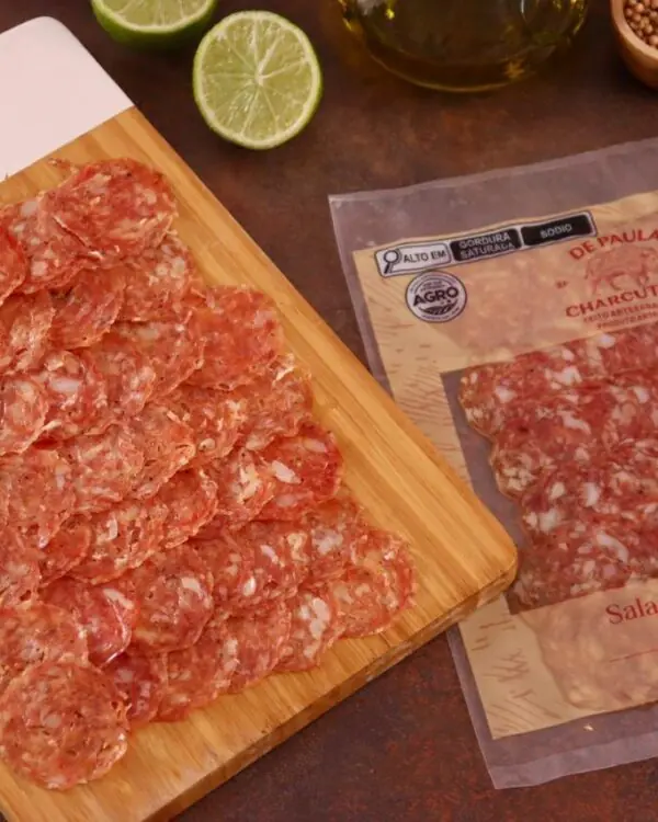 Fatias de Salame Toscano dispostas em tábua de bambu gourmet com limão e alecrim ao fundo. Fatias de Salame Toscano dispostas em tábua de bambu gourmet com limão e alecrim ao fundo.