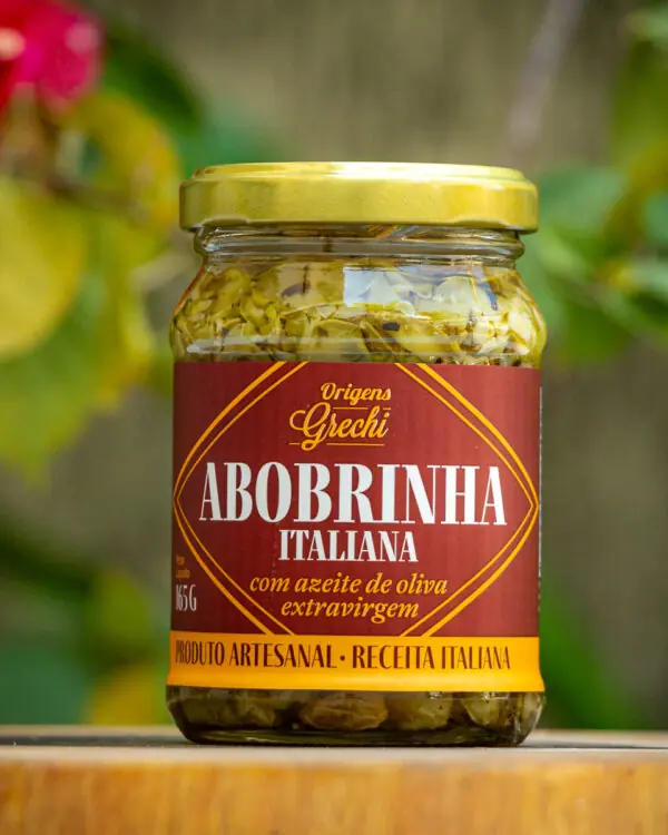 Pote de abobrinha italiana Origens Grechi 165g com rótulo bordô e tampa dourada sobre tábua de madeira