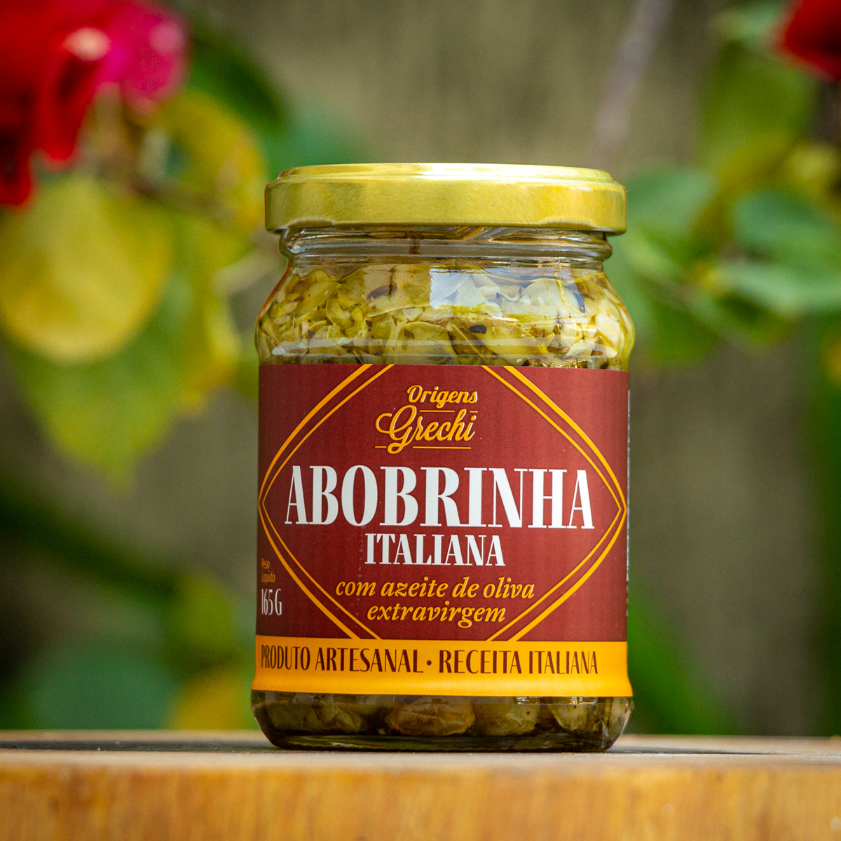 Pote de abobrinha italiana Origens Grechi 165g com rótulo bordô e tampa dourada sobre tábua de madeira