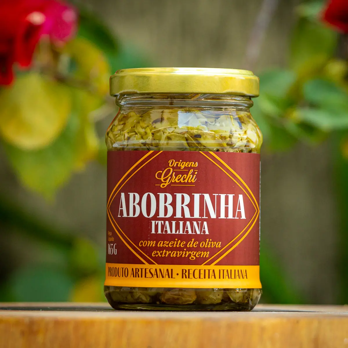 Pote de abobrinha italiana Origens Grechi 165g com rótulo bordô e tampa dourada sobre tábua de madeira