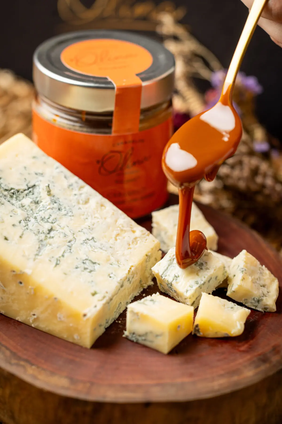 Calda de caramelo de chocolate e laranja sendo despejada sobre queijo gorgonzola em tábua rústica.