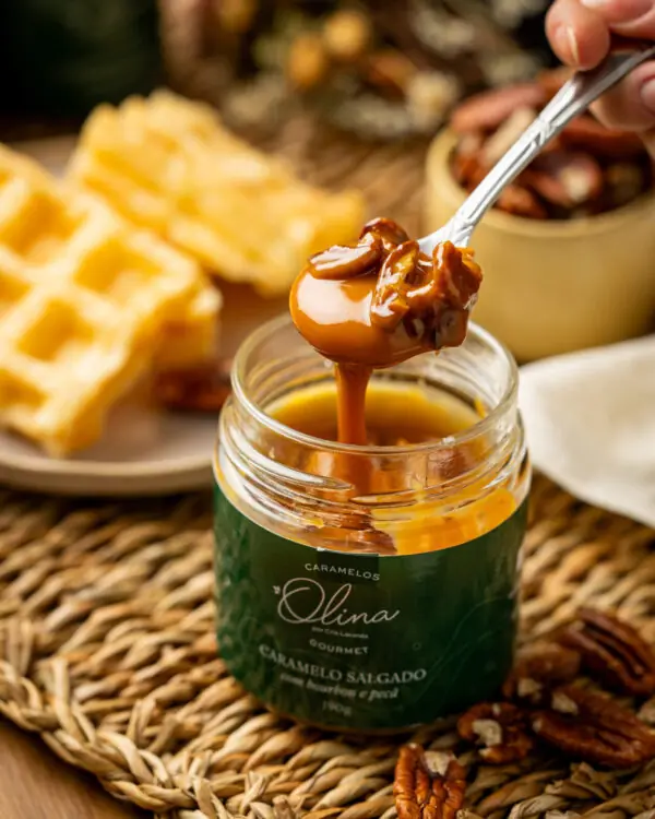 Imagem macro atrativa focando em abastada colher prateada segurando calda densa e grandes castanhas sobre pote de Bourbon Olina ladeando os doces waffles do lanche da tarde agradáveis ao sol e um copo de pécãs puras cruas soltas. Imagem macro atrativa focando em abastada colher prateada segurando calda densa e grandes castanhas sobre pote de Bourbon Olina ladeando os doces waffles do lanche da tarde agradáveis ao sol e um copo de pécãs puras cruas soltas.