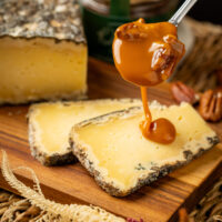 inâmica da Calda de caramelo rústico e doce amadeirada despejada graciosamente por cima das fatias amarelas pontilhadas do puro queijo curado, servido acima da base tabulada de carne natural rústica.