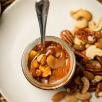 Visão do interior do pote escuro de caramelo Olina mostrando o preenchimento volumoso com pedaços maciços de castanhas variadas.
