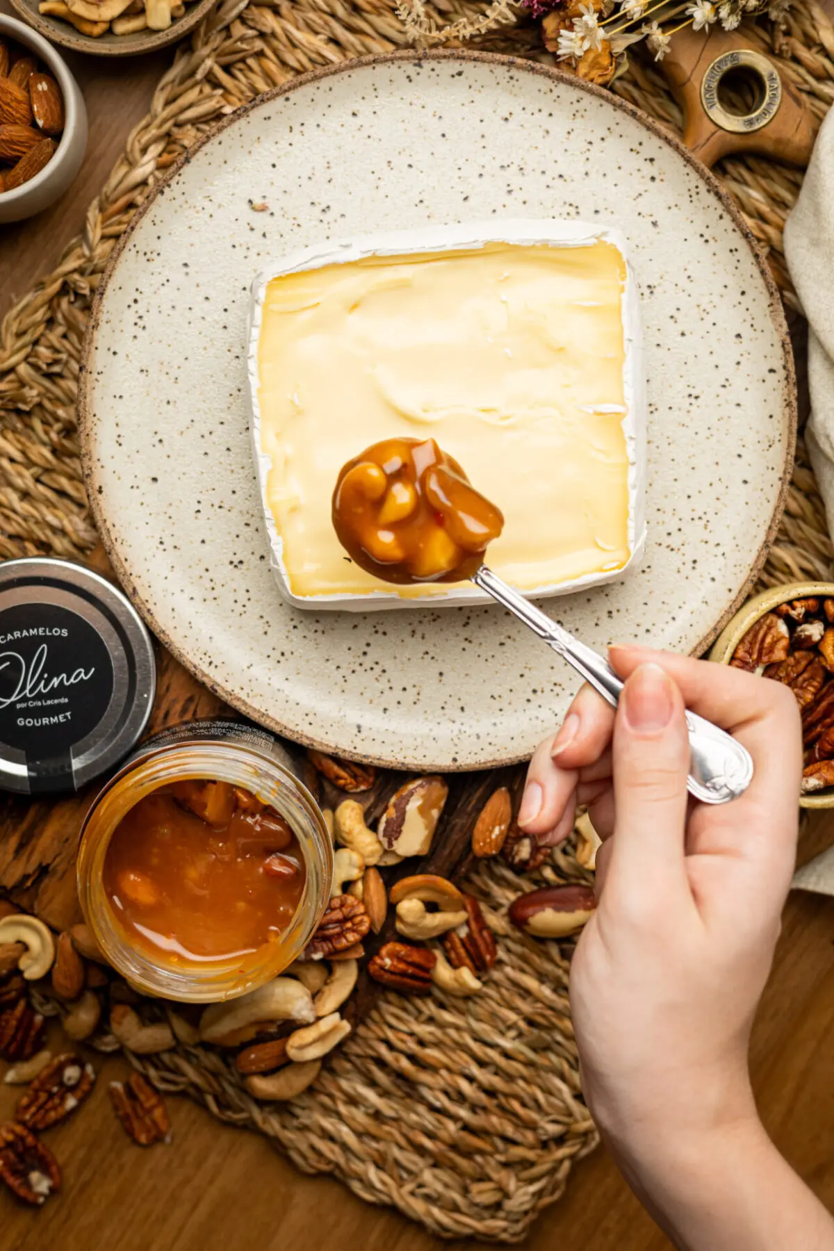 Calda cremosa de caramelo picante e pedaços de nozes caindo devagar sobre fatia rústica de queijo brie macio.