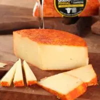536c6500f68c813a6f61914346e50f16.jpg Queijo Pinhal maturação longa cortado com fatias tábua de madeira vinho tinto ao fundo