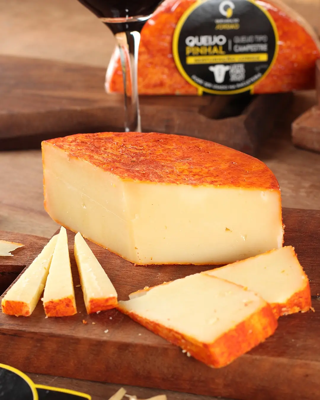 536c6500f68c813a6f61914346e50f16.jpg Queijo Pinhal maturação longa cortado com fatias tábua de madeira vinho tinto ao fundo