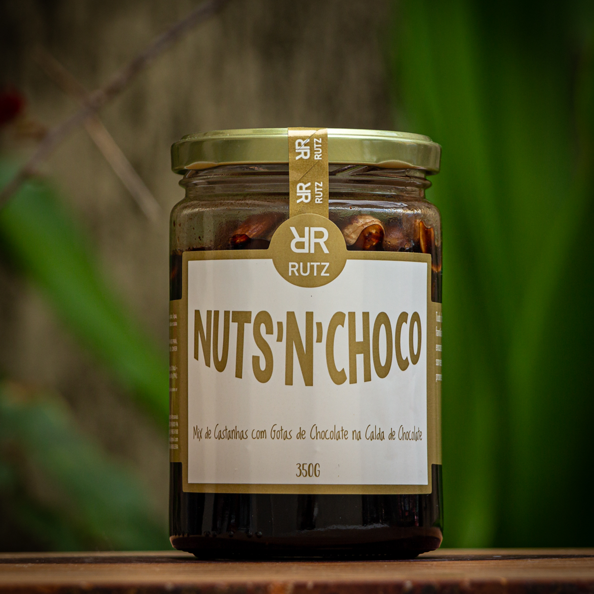 Pote de vidro do mix de castanhas com chocolate Nuts'n Choco Rutz 350g sobre mesa de madeira.