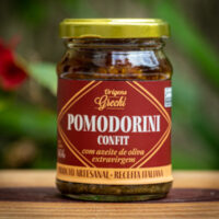 ote de Pomodorini Confit Origens Grechi sobre madeira rústica, evidenciando o tomate cereja confit artesanal.