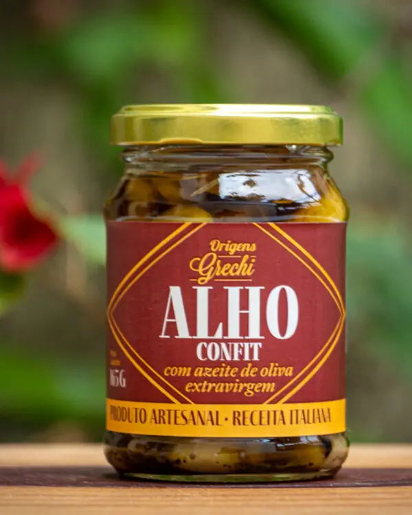Pote de Alho Confit Origens Grechi sobre madeira rústica, destacando o alho confitado artesanal em azeite.