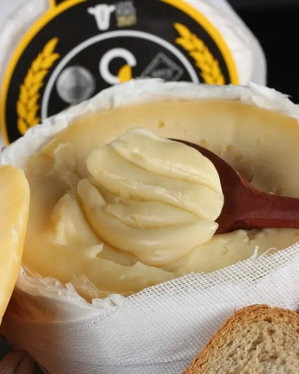 Queijo do Jordão Pasta Mole aberto textura ultra-cremosa colher de madeira com pães artesanais